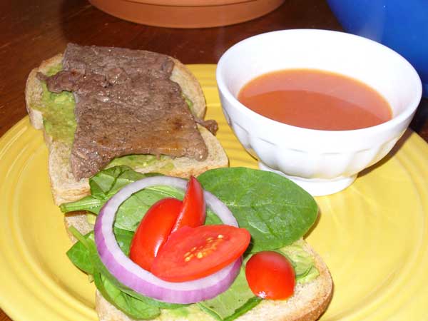 Steak, spinach, onion, tomato, and avacado sandwich, with bowl of tomato soup.